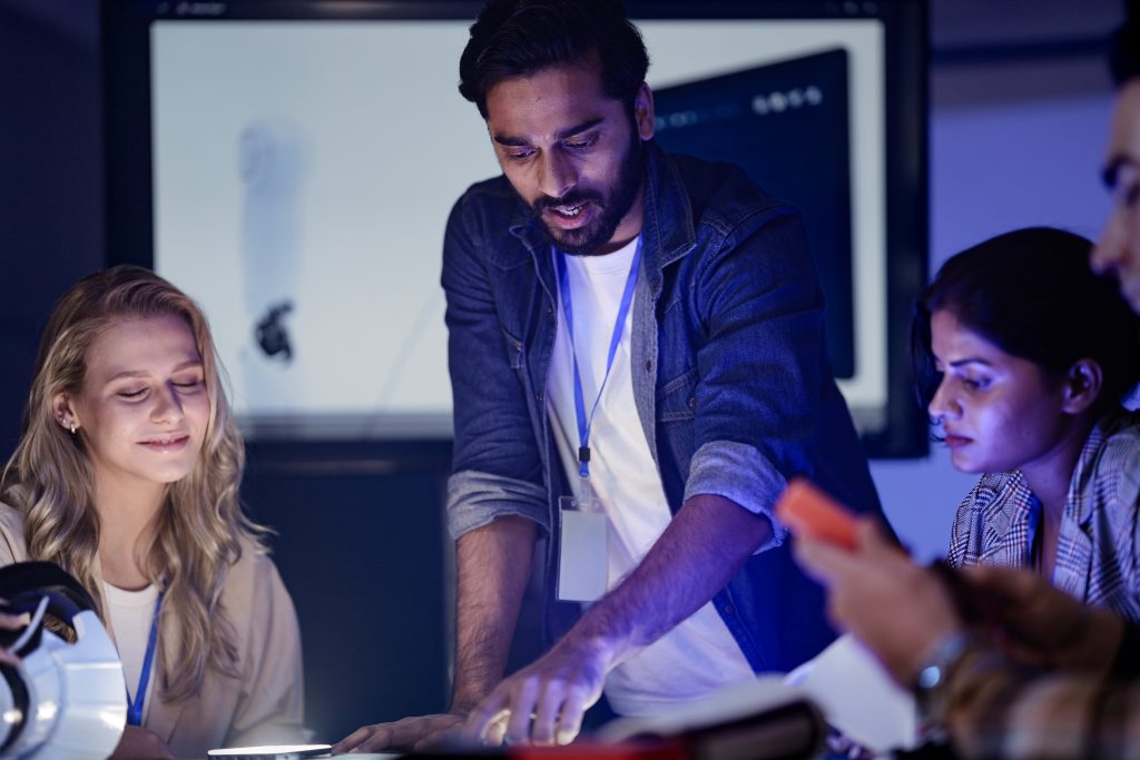 An Indian engineer presents an AI powered prosthetic arm in an RD lab. Her team, including a Caucasian woman, analyzes the robotic prototype and its data on a screen.